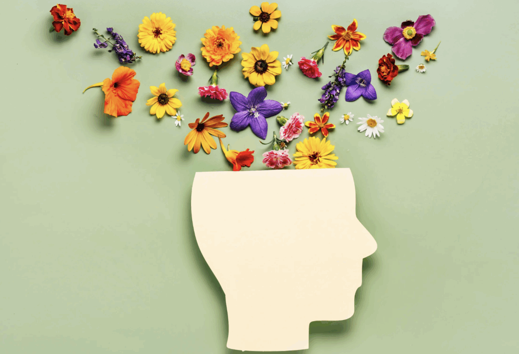 Silhouette of a human head with colorful flowers emerging from the top, symbolizing mental health, growth, and emotional well-being